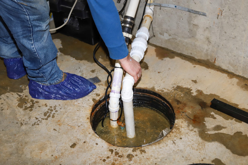 Plumber repairing failing sump pump in a flooding basement