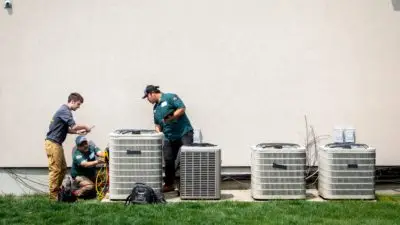 HomeWorks Energy team performs a cooling checkup at a customer's home, standing by a large air conditioner.