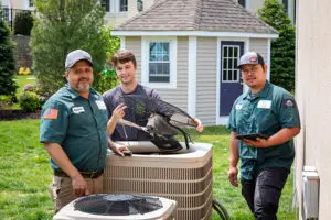 HomeWorks Energy team performs a cooling checkup at a customer's home, standing by a large air conditioner.