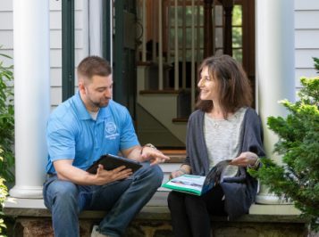 A man and woman relax on their porch, discussing home energy assessments with Homeworks Energy, a Mass Save partne