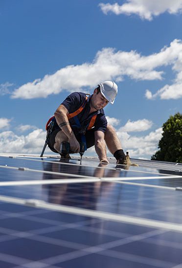 Solar panel technician with drill installing solar panels on roof on a sunny day