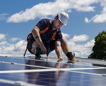 Solar panel technician with drill installing solar panels on roof on a sunny day