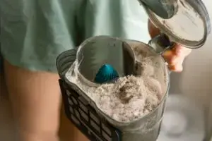 Woman holding full vacuum container of dust dirt and pollen brought in from spring allergies that can be prevented by installing new insulation with a professional energy efficiency provider