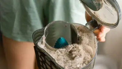 Woman holding full vacuum container of dust dirt and pollen brought in from spring allergies that can be prevented by installing new insulation with a professional energy efficiency provider